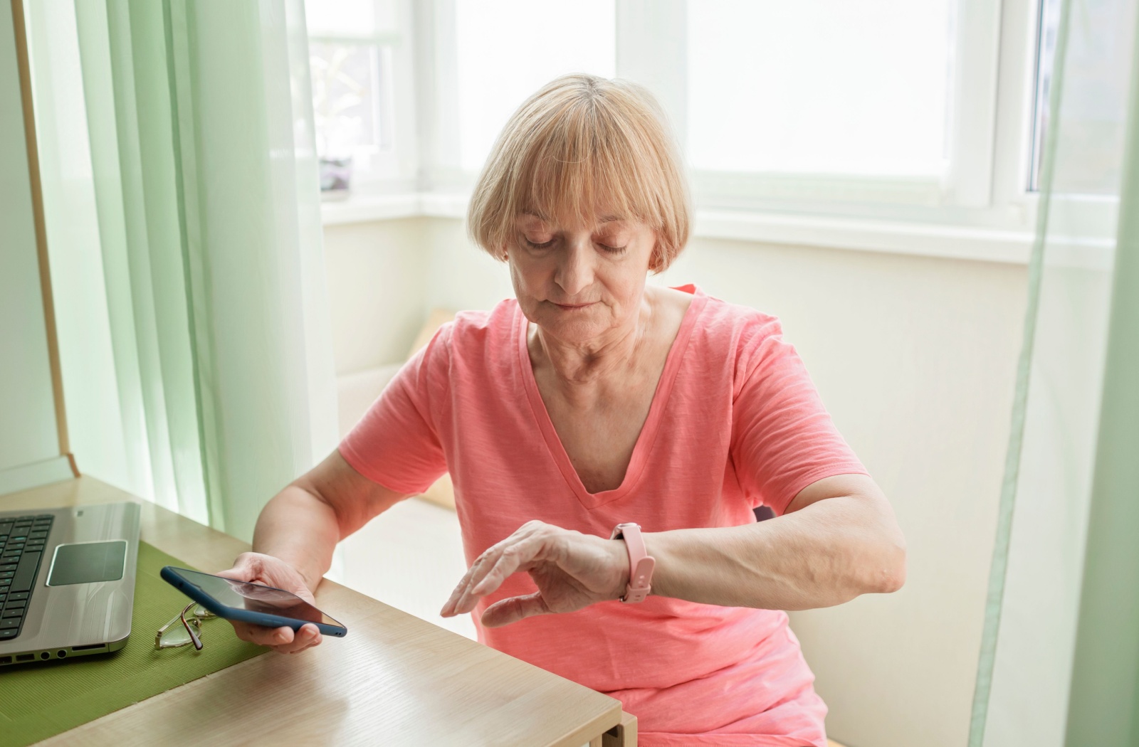 An older adult checking her health information while looking at her smart watch on her left hand  and holding her phone in her right hand.