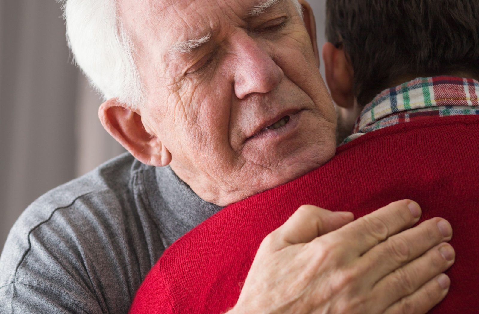 A close up of an older adult with their eyes closed hugging their adult child.
