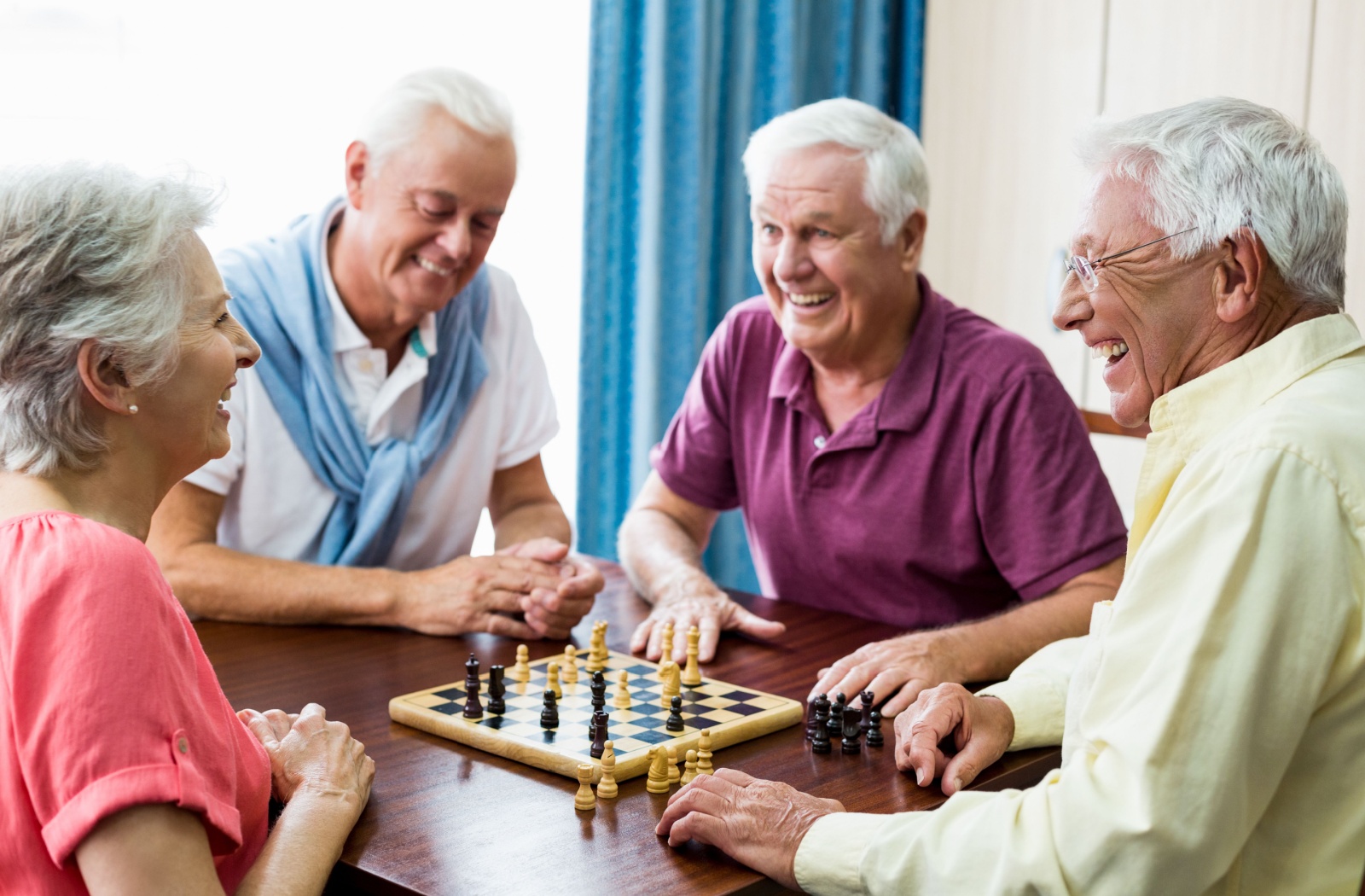 A group of four seniors smiling and playing chess together