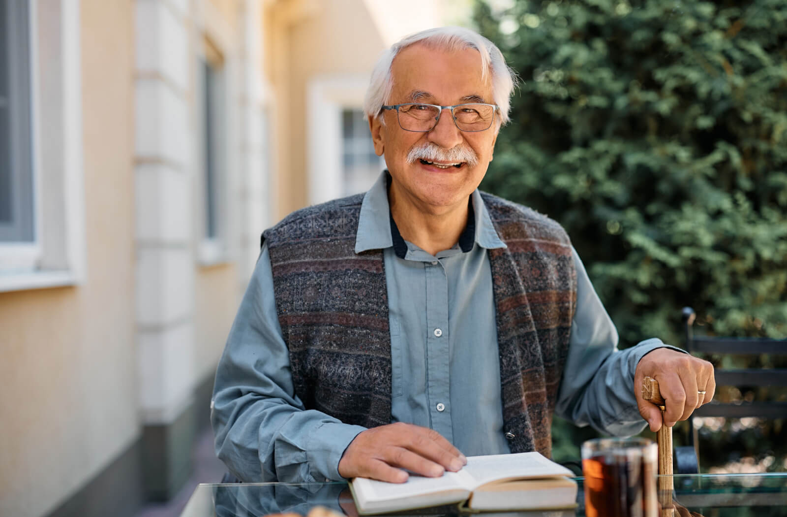 An older adult in assisted living sitting outside with a book and smiling after rediscovering their independence.