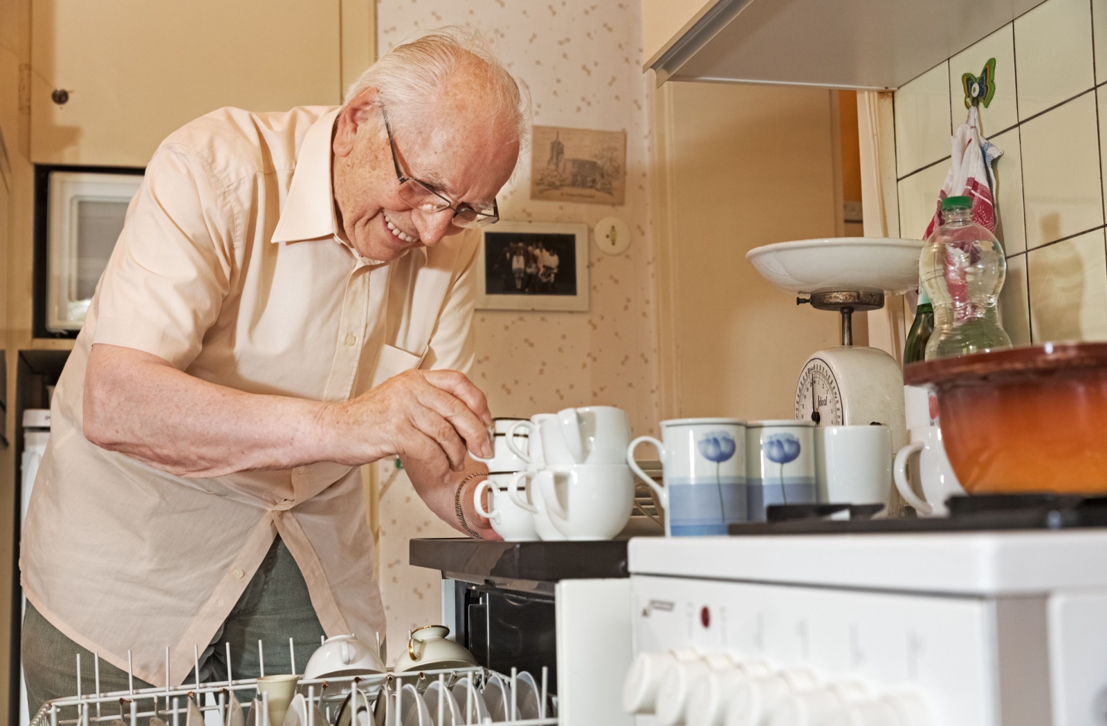 A smiling senior unloads the dishwasher in his independent living apartment.