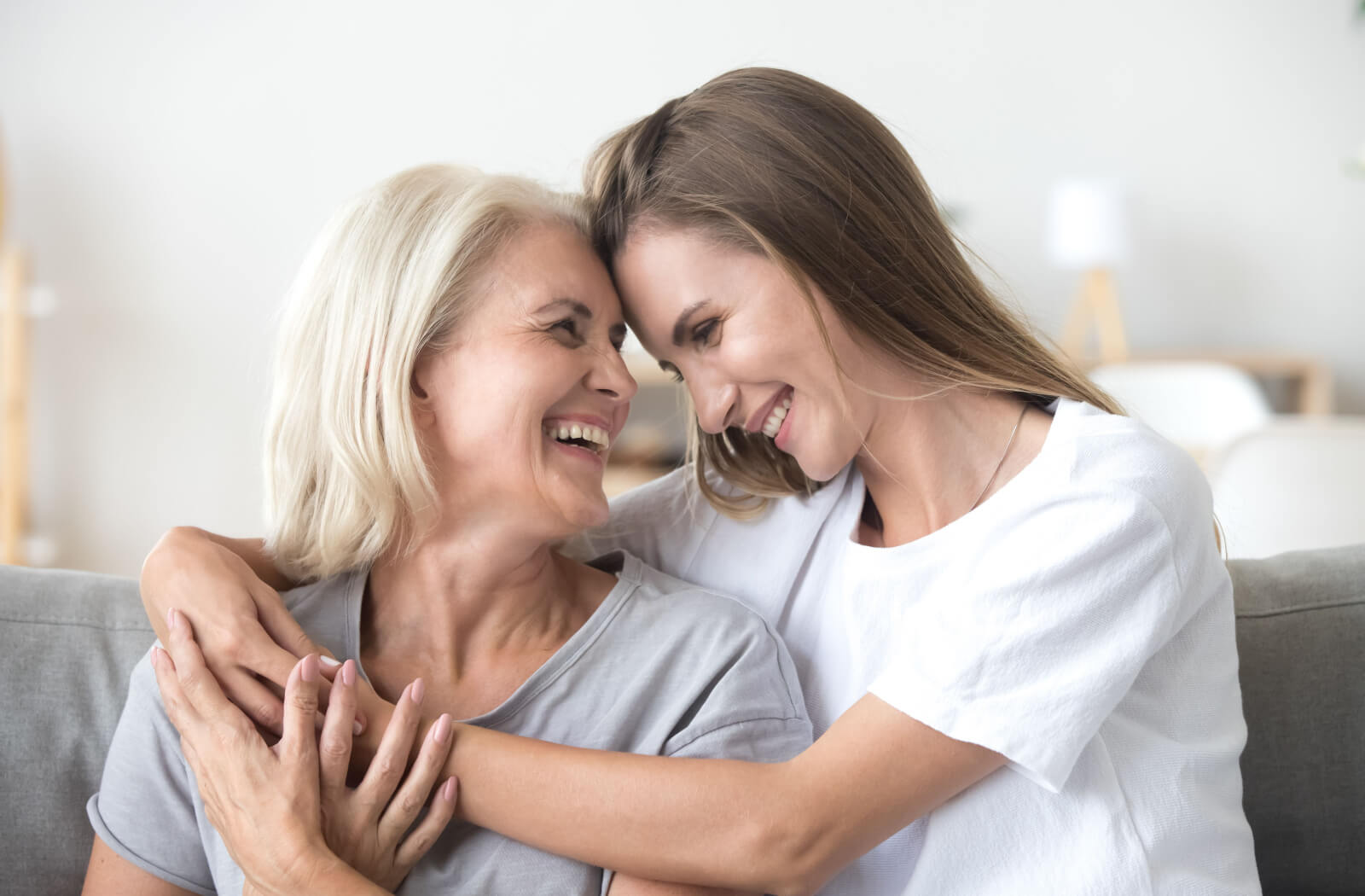 An adult child hugging their parent with Alzheimer's disease on the couch as they laugh together.