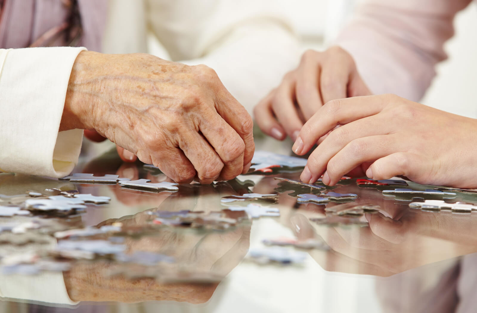 A close-up image of an older adult's hands as they fit together a puzzle with a caregiver.