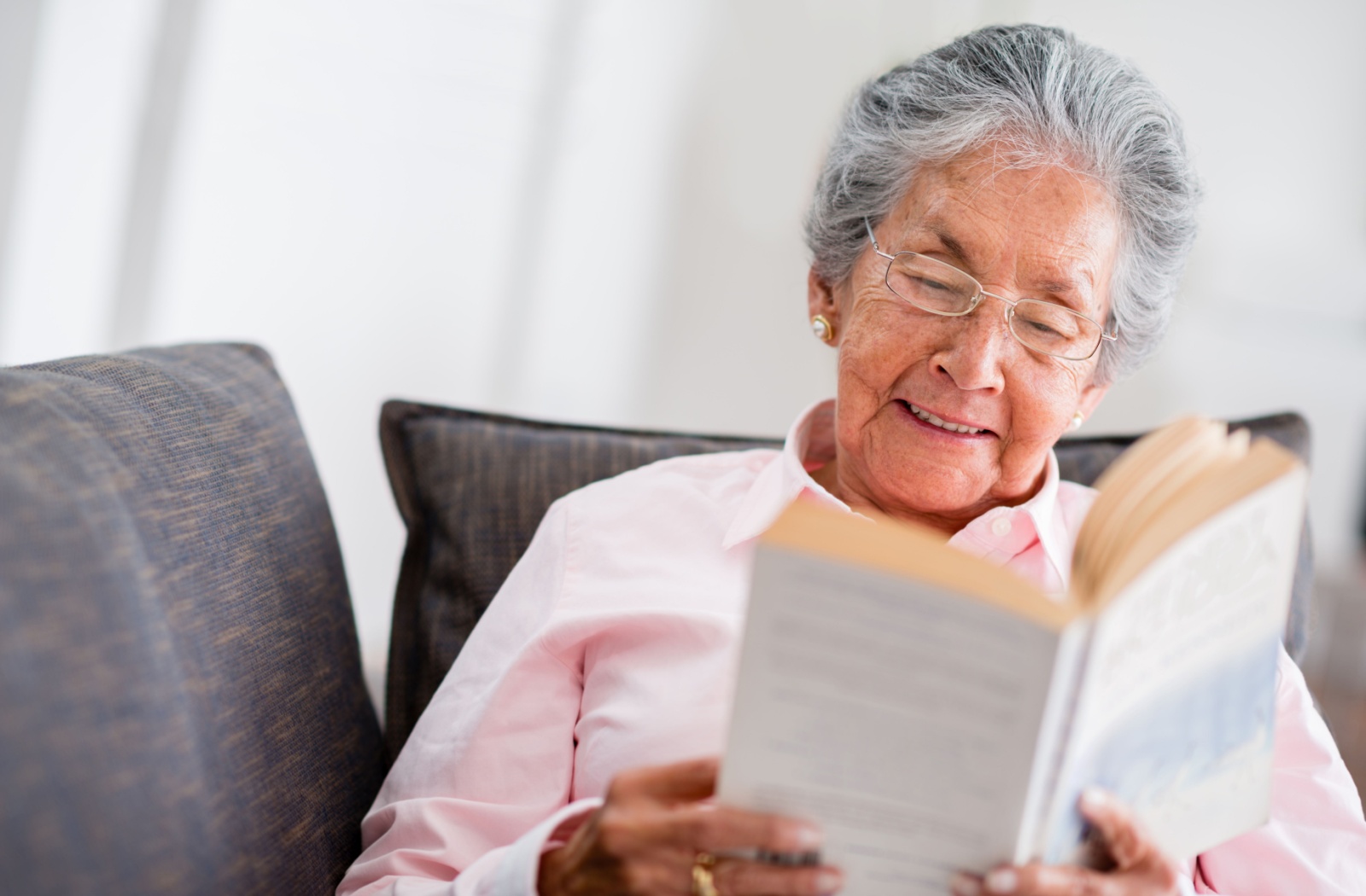 Older adult reading a book on a cushioned couch with soft lighting and a calm, focused expression