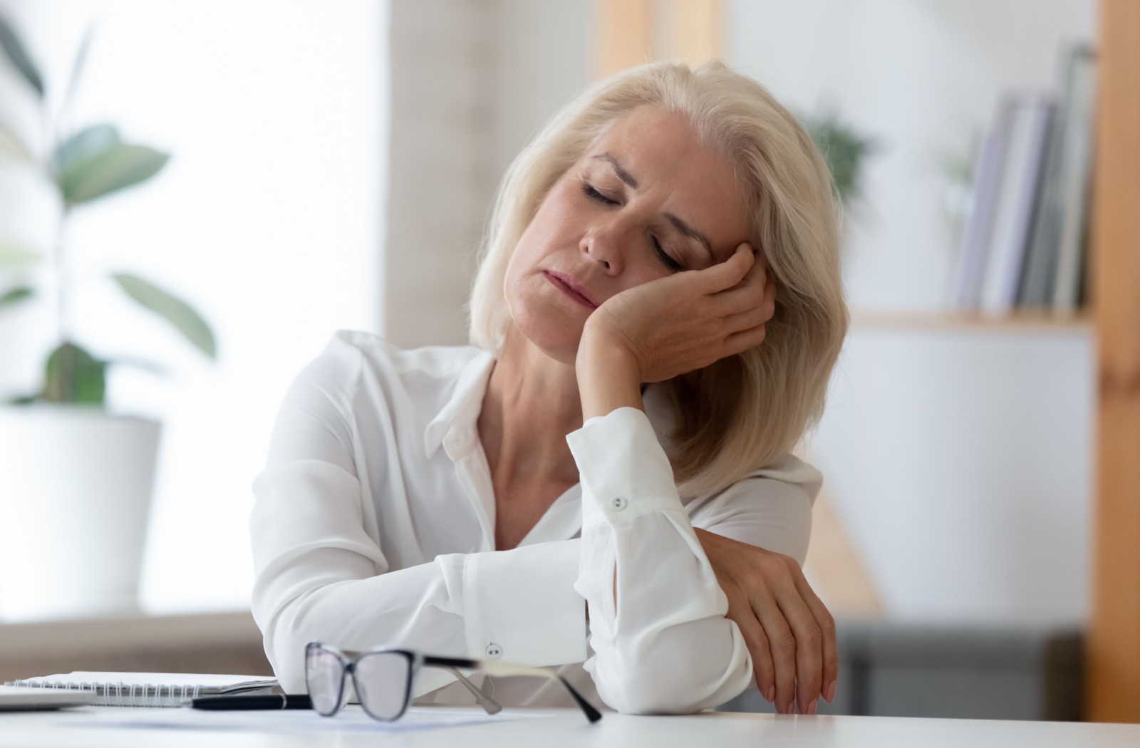 An exhausted senior sits at a desk, having fallen asleep, feeling extreme fatigue.
