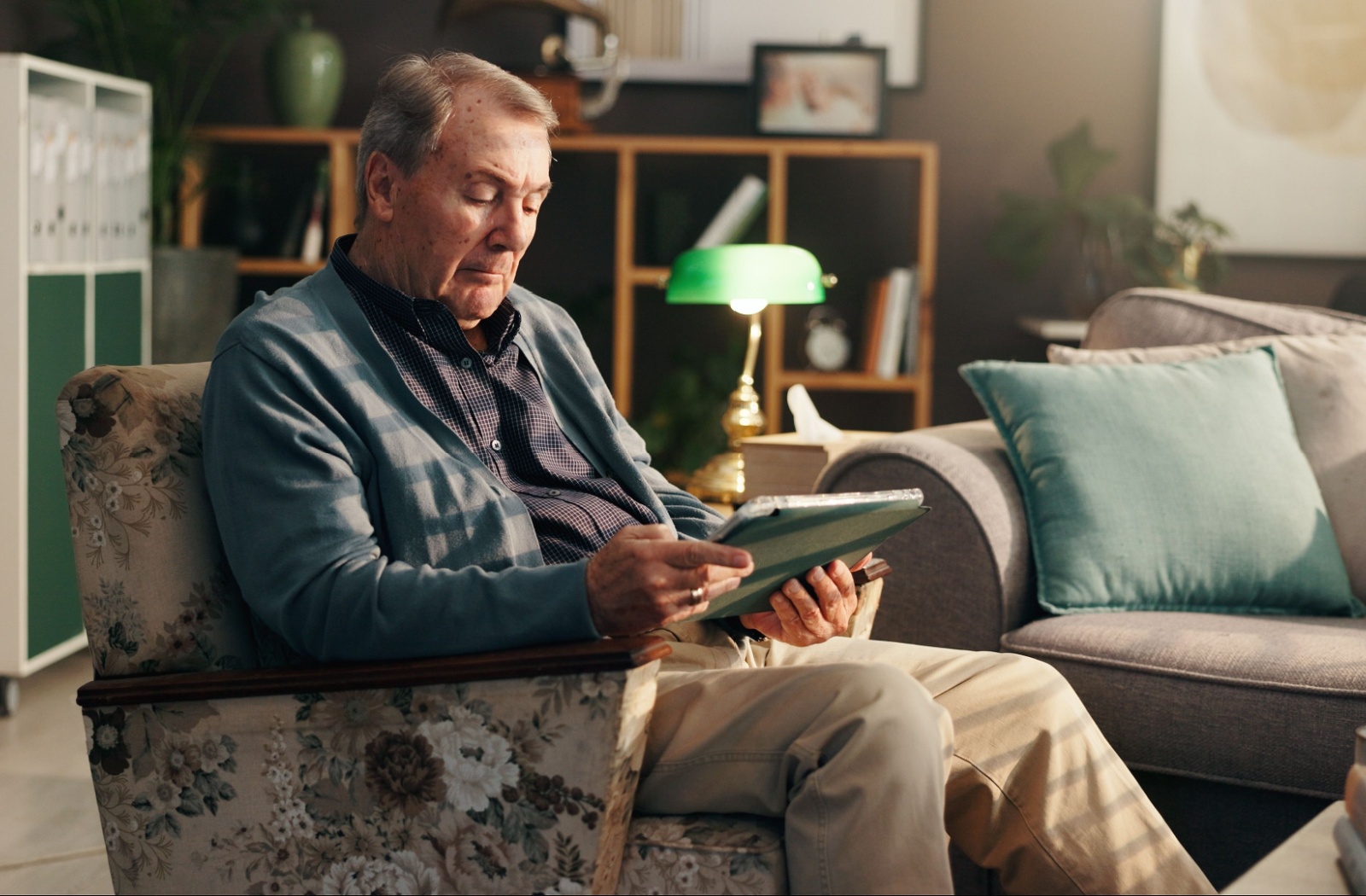 A senior sits on an armchair and watches a movie on a tablet computer.